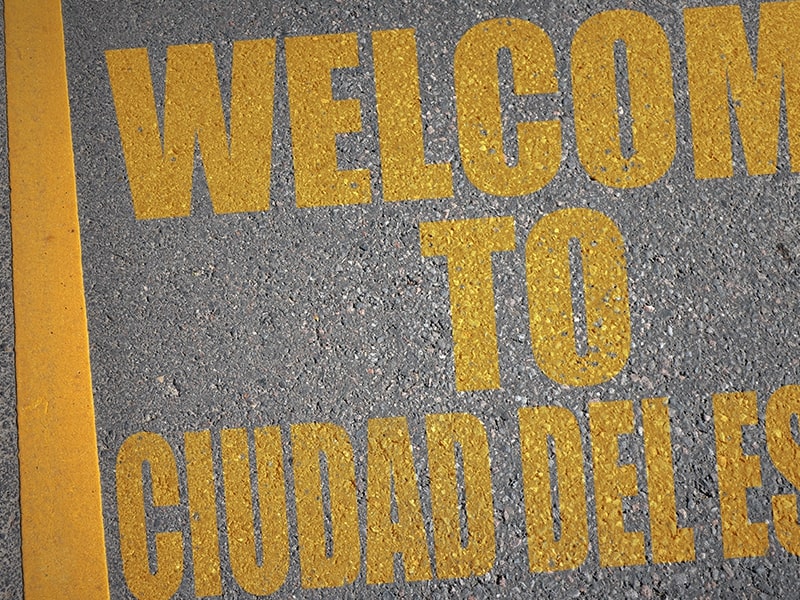 Sinalização de solo com a mensagem "Welcome to Ciudad del Este" pintada em amarelo sobre asfalto, marcando a entrada na cidade de Ciudad del Este no Paraguai, ideal para quem está viajando para o Paraguai a partir de Foz do Iguaçu.