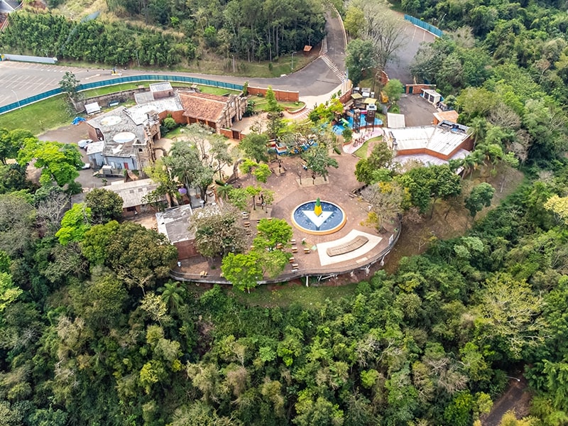 Vista aérea do Marco das Três Fronteiras, onde Brasil, Paraguai e Argentina se encontram, cercado por uma densa vegetação e uma área turística.