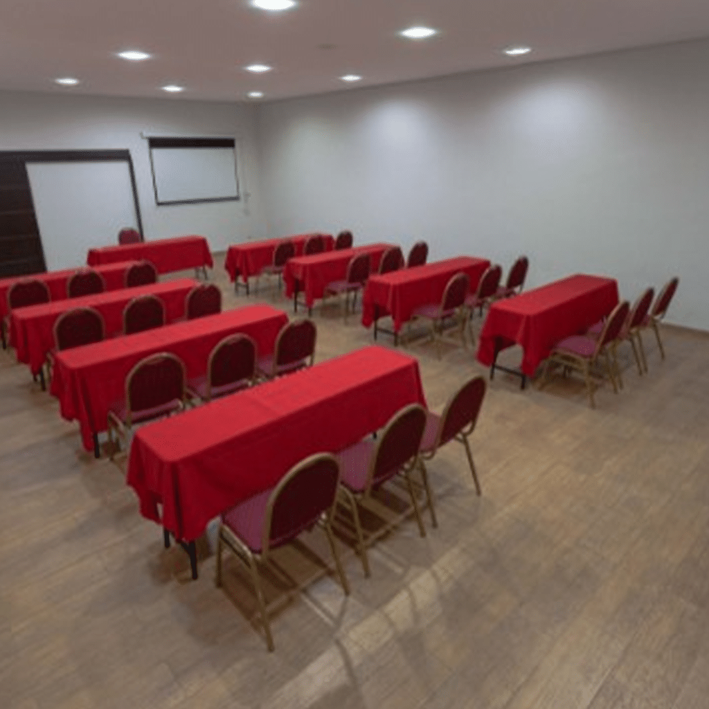 Sala de reuniões com várias mesas cobertas de vermelho, layout voltado para treinamentos.