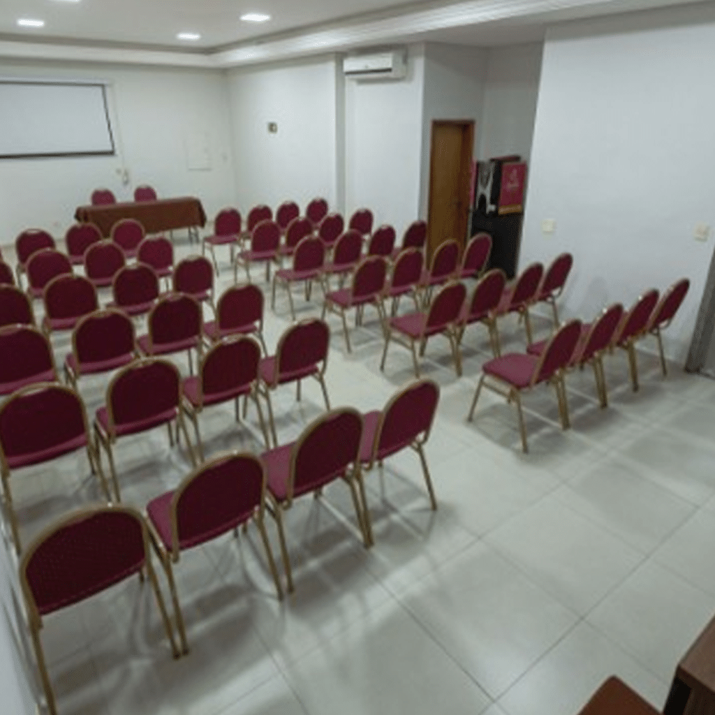 Sala de reuniões com várias mesas cobertas de vermelho, layout voltado para treinamentos.